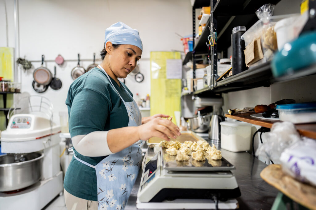 Kitchen staff member carefully weighing dough in a restaurant kitchen.